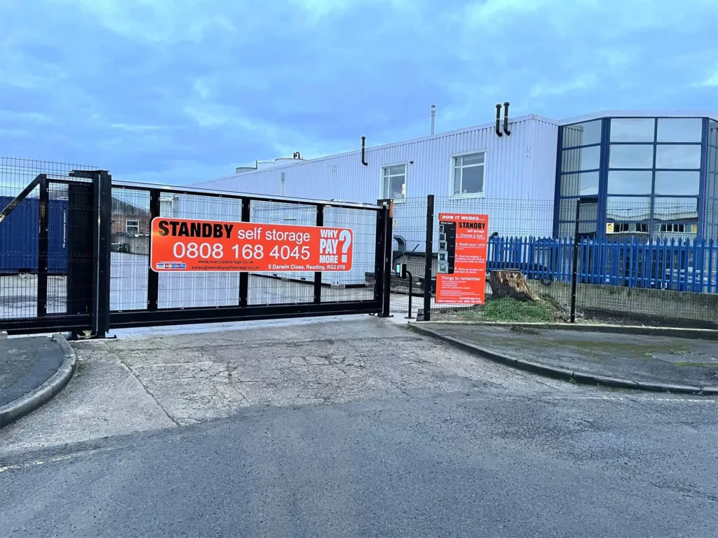 A gated self-storage facility, "Standby Self Storage," displays its name and contact number 0808 168 4045. The facility is visible behind the gate, flanked by a sidewalk and street under a cloudy sky. Ideal for student storage, it offers secure self storage containers for all needs.